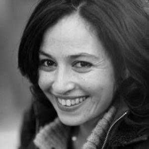 A black and white photograph of Hind Saïh smiling at the camera, with a blurry background.
