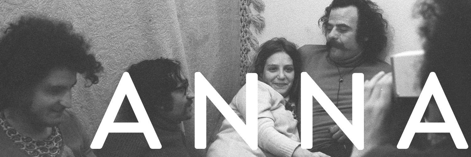 Film Still: A young woman sitting in the middle of a group of 4 men. The film title, Anna, is in the right corner.