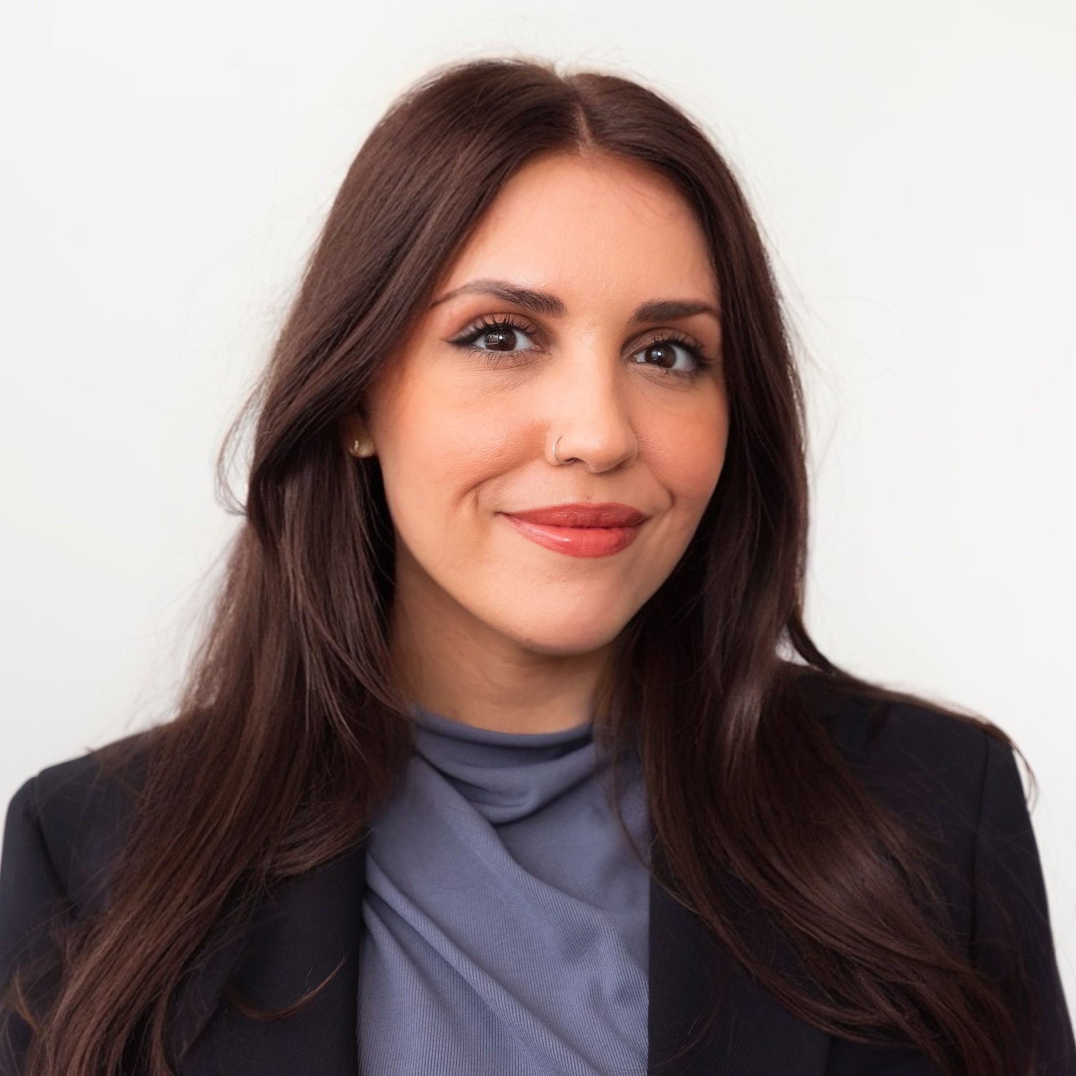 Photo of a person with long brown hair, wearing a blazer and a blue-grey shirt.