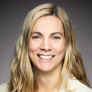 A photograph of the Honourable Pascale St-Onge, a white woman with long blonde hair, as she smiles at the camera against a grey backdrop.