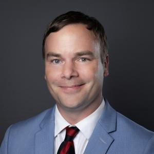 Photo of a man in a suit with short brown hair.